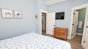 Un dormitorio con cama, cómoda de madera, televisor y dos puertas que dan a otras habitaciones.