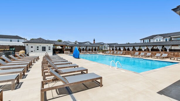 Zona de piscina con sillones de descanso y un pequeño edificio, probablemente un bar junto a la piscina o vestuario.