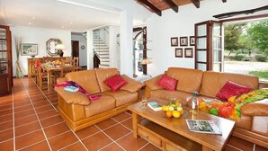 A living room with two brown leather sofas, a wooden coffee table with fruits and a magazine, and a dining area in the background. - Villa 'Colet Vell' with Private Pool, Wi-Fi and Air Conditioning (Illes Balears)