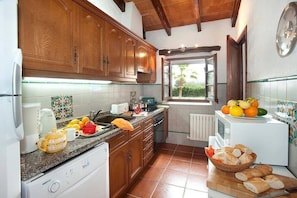 A kitchen with wooden cabinets, a sink, a window, a refrigerator, and a countertop with fruits and bread.