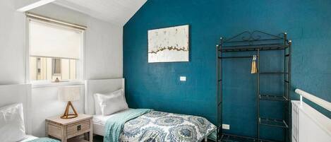 A bedroom with two beds, a window with blinds, a wall-mounted shelf, and a ceiling with exposed beams.