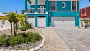 A two-story house with a garage, a balcony, and a small garden area with palm trees. - 155 Inn-2-Blue: Poolside Fun & Beach Walks Await! (Fort Myers Beach)