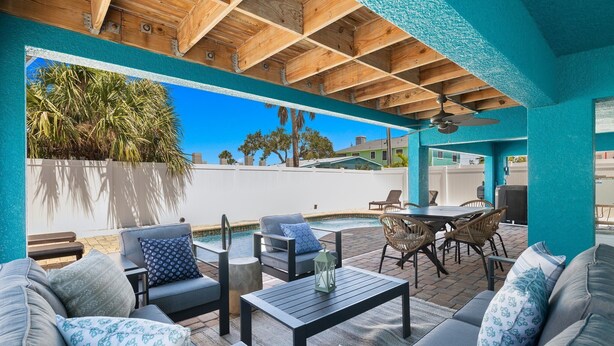 An outdoor patio with wooden ceiling beams, a pool, and seating areas with cushions and tables. - 155 Inn-2-Blue: Poolside Fun & Beach Walks Await! (Fort Myers Beach)