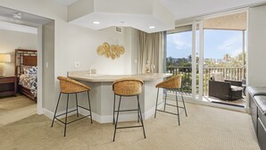 A modern kitchen with a bar area, two wicker barstools, and a large sliding glass door leading to a balcony with outdoor furniture. - Family Beach Condo | 3BR, Pickleball, BBQ & Prime Location (Fort Myers Beach)