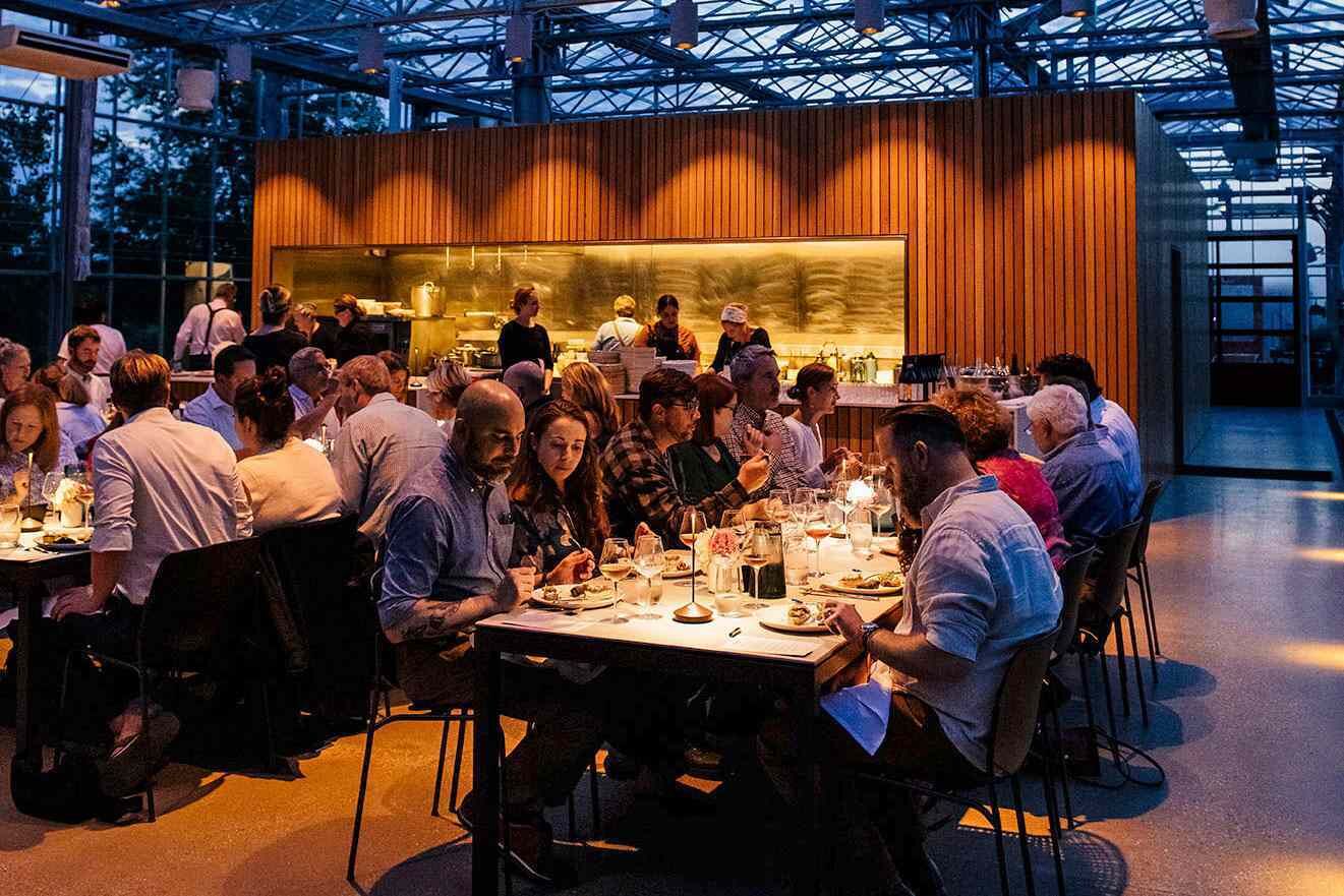 A modern restaurant with a high ceiling and wooden paneling, featuring tables set for dining.