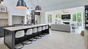 A modern kitchen with a central island, bar stools, and a dining area with a sofa.