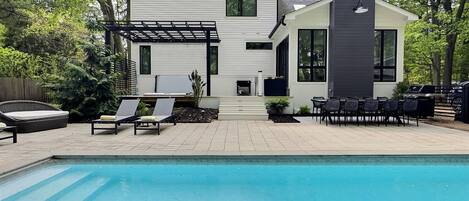 A modern house with a pool, outdoor seating, and a pergola.