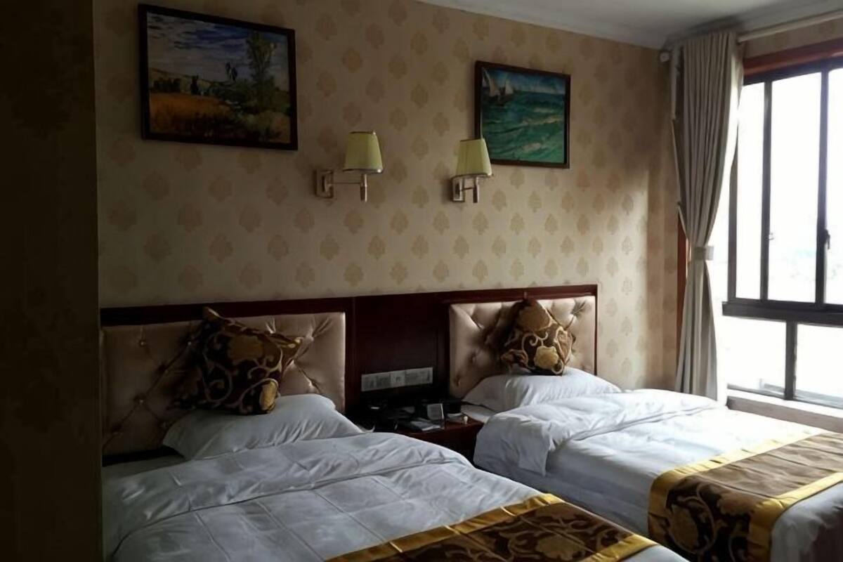 Une chambre d’hôtel avec deux lits, une tête de lit, des lampes fixées au mur et une fenêtre avec des rideaux.