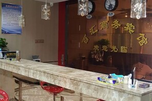 Un mostrador de recepción con un reloj, un tablón de anuncios y una ventana con caracteres chinos.