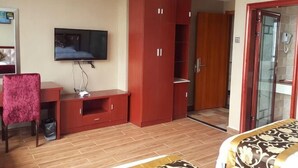 Hotellihuone, jossa on televisio, punainen vaatekaappi, työpöytä ja sänky.