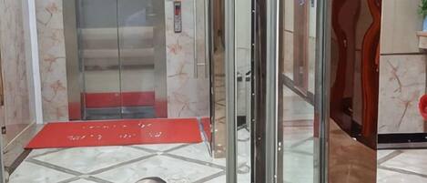 A hotel lobby with a glass elevator, a patterned floor, and a red carpet.