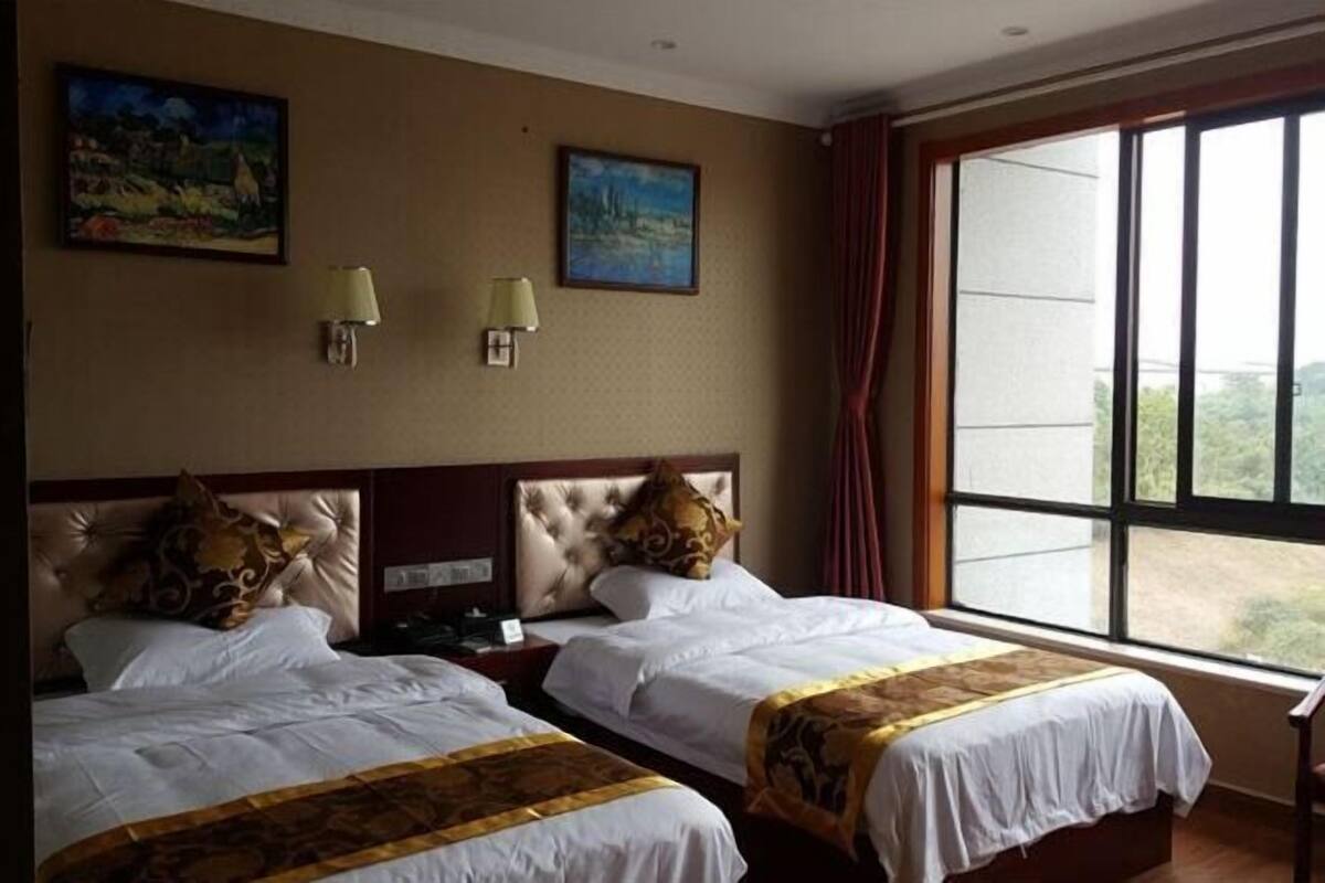 Une chambre d’hôtel avec deux lits, une grande fenêtre et deux lampes fixées au mur.