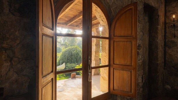 Una habitación con paredes de piedra, un ventanal arqueado grande, piso de madera y una pequeña mesa.