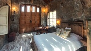 Una habitación rústica de piedra con techo de madera, una cama con almohadas, una mesa con sillas y una pared de piedra.