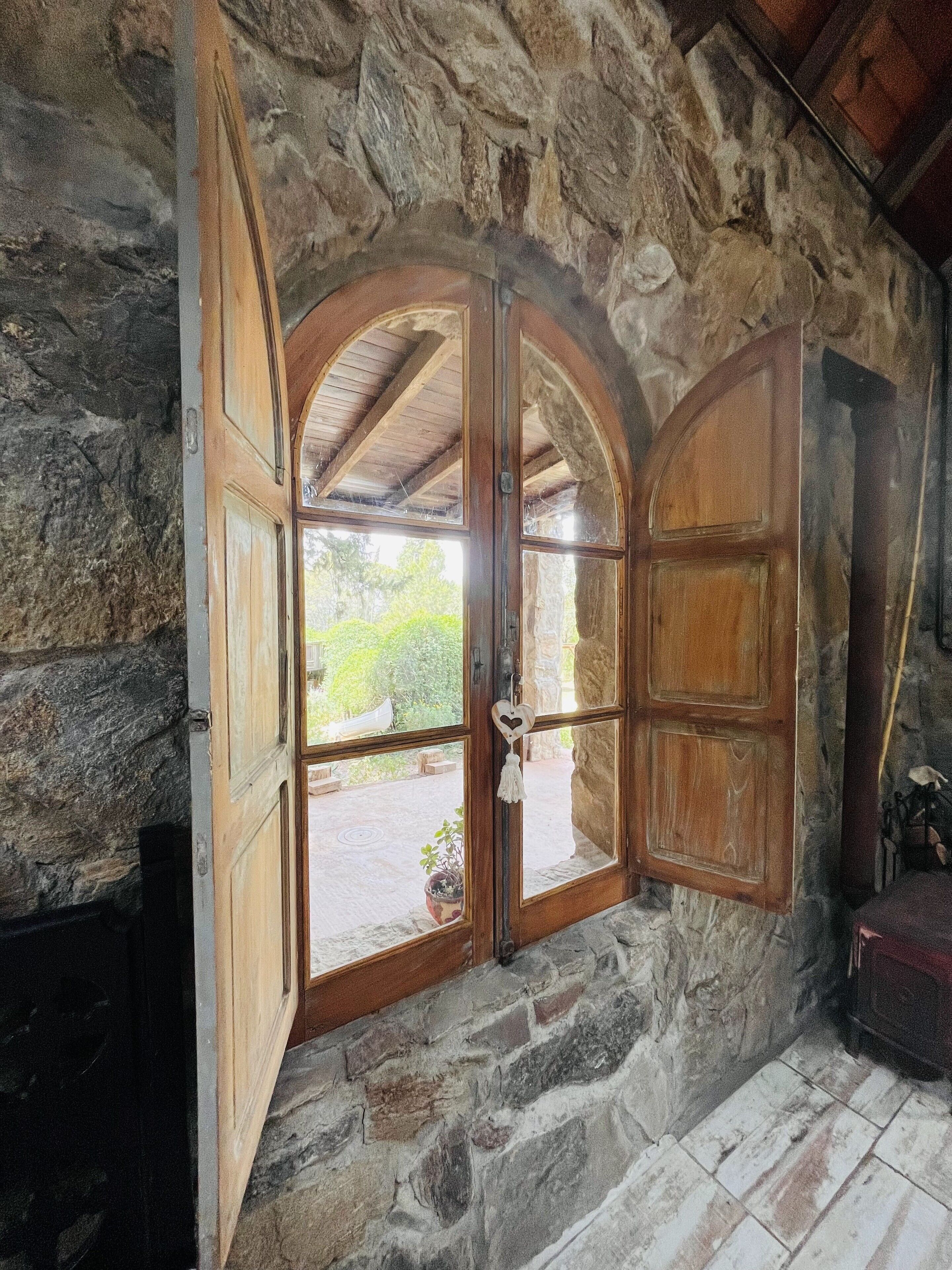 A stone-walled room with a large arched window and wooden shutters.