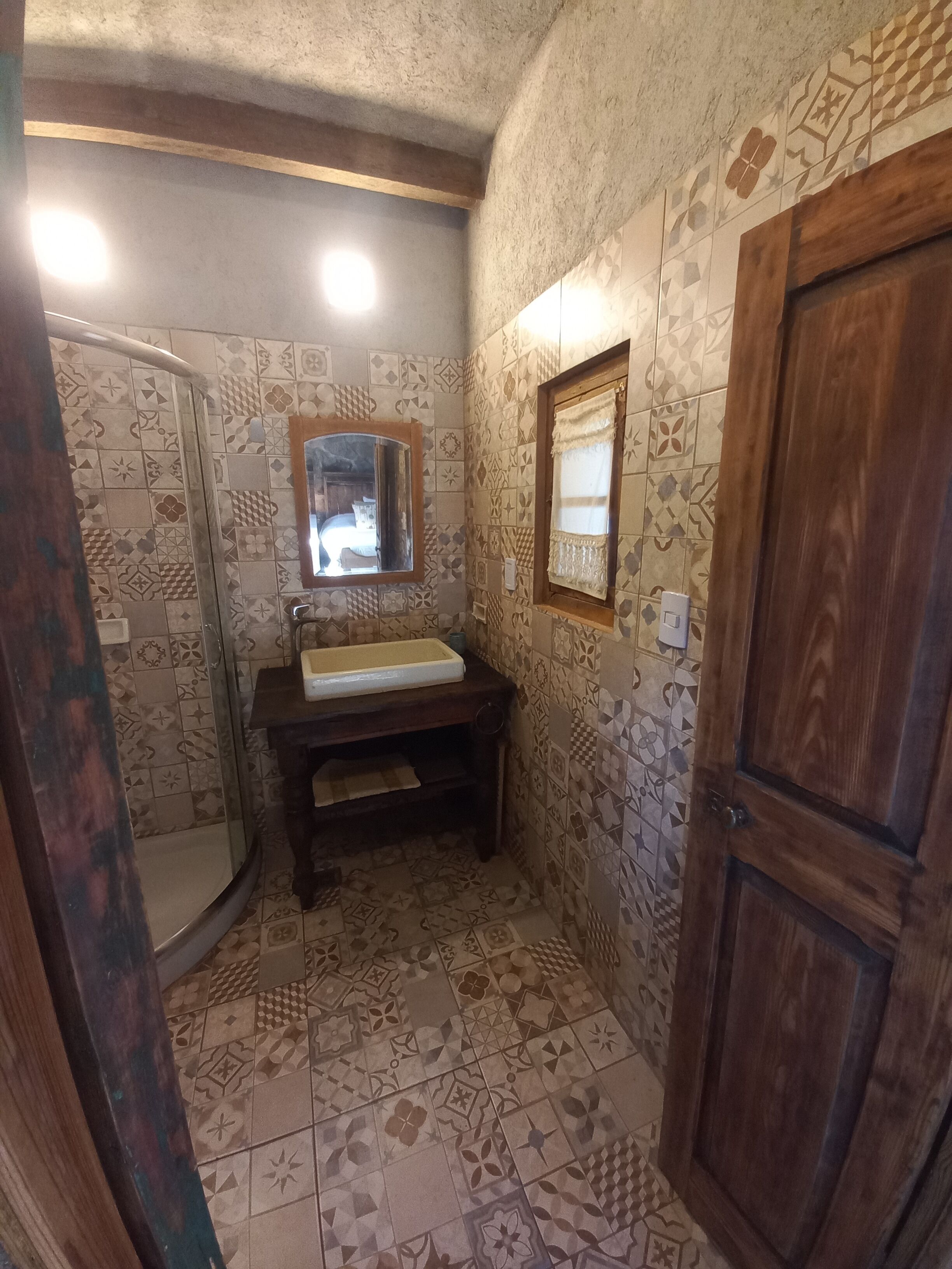 A bathroom with patterned tiles, a wooden vanity, a mirror, and a shower area.