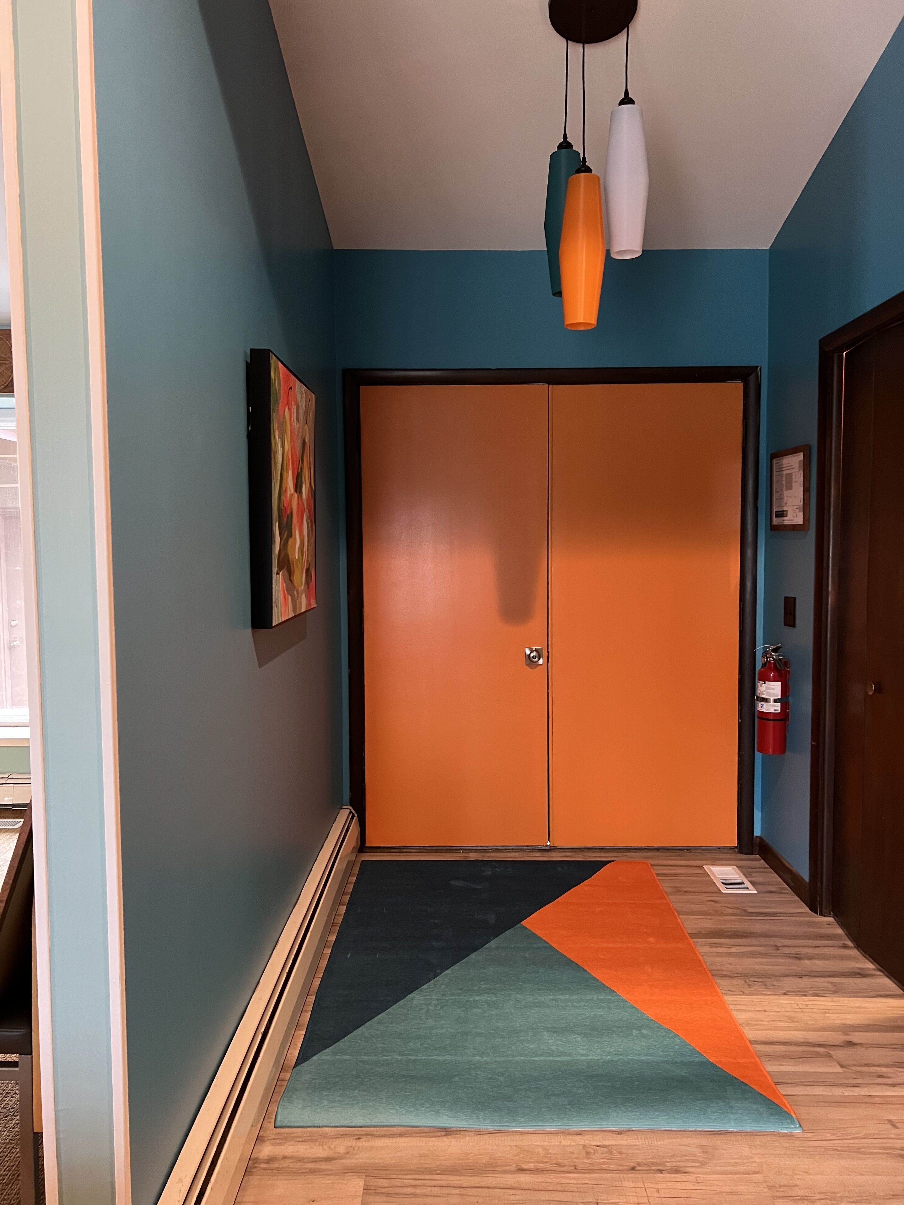 Un couloir avec un plancher en bois, un tapis coloré, un mur bleu et une porte sur laquelle est fixé un extincteur.