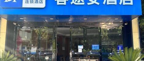 A hotel entrance with a blue sign, glass doors, and potted plants outside.