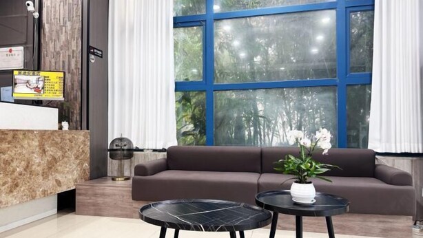 A modern reception area with a marble counter, a brown sofa, two black tables, and a large window with blue framing. - Ketouan Hotel (Yangzhou Slender West Lake Branch) (Yangzhou)