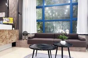 A modern reception area with a marble counter, a brown sofa, two black tables, and a large window with blue framing. - Ketouan Hotel (Yangzhou Slender West Lake Branch) (Yangzhou)