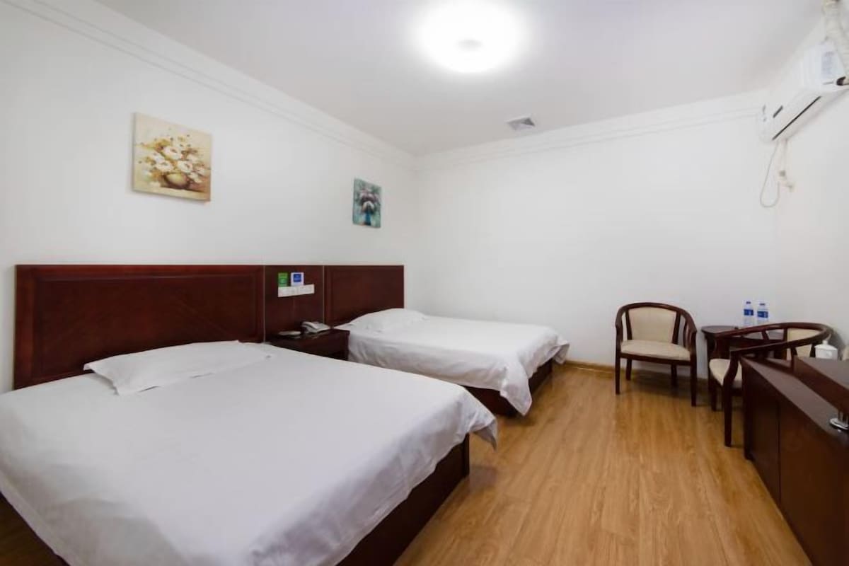 A hotel room with two single beds, a wooden headboard, a desk with a chair, and a small table with two bottles.