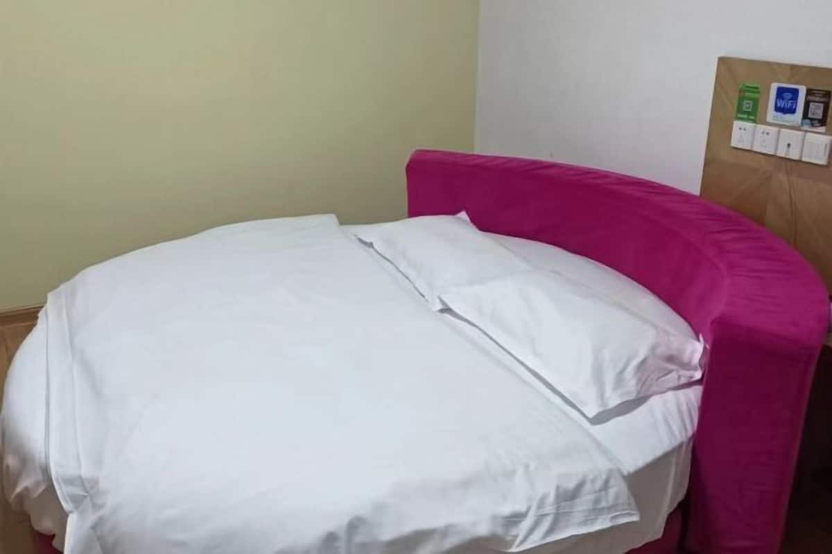 A bed with white bedding and a pink headboard in a room with a bulletin board on the wall.