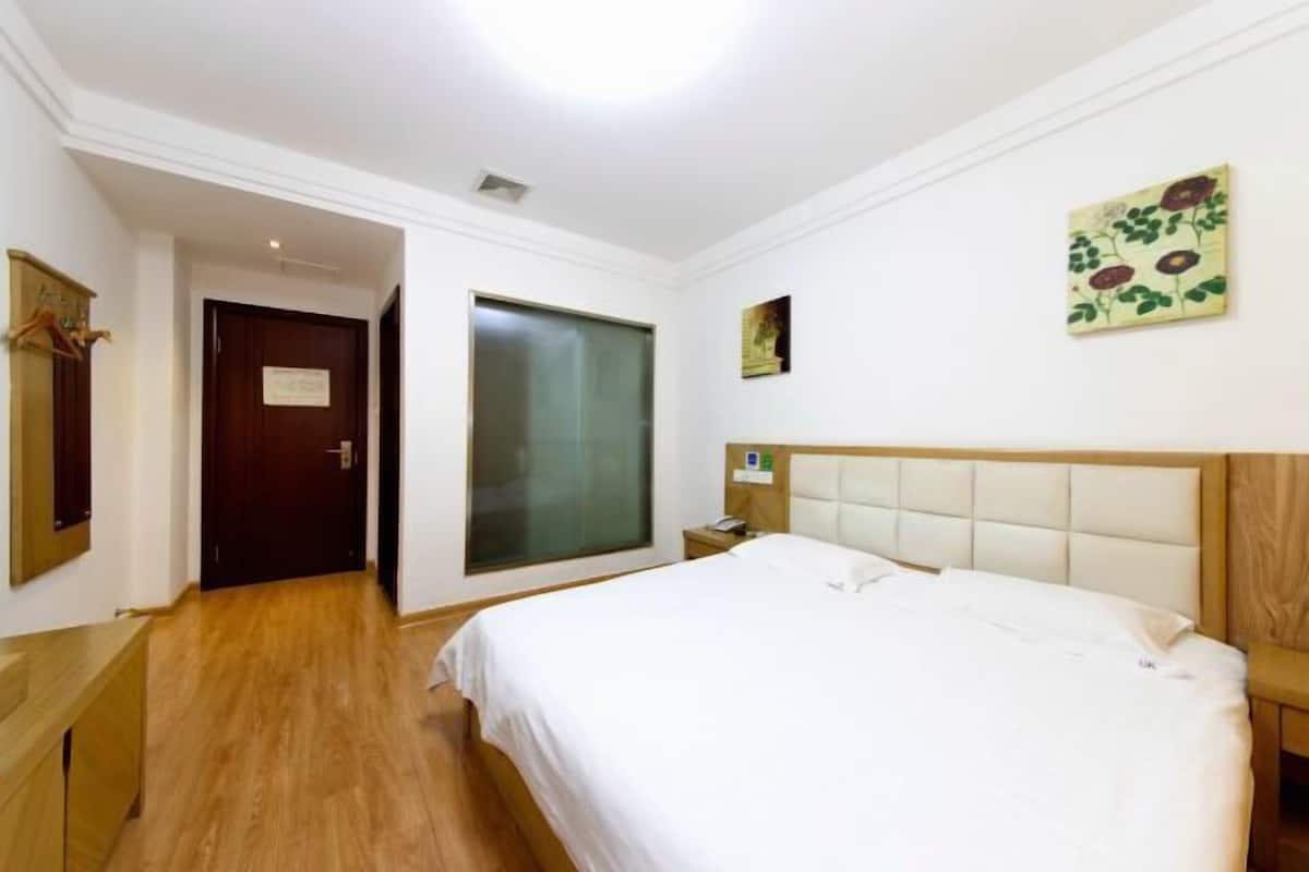 A hotel room with a bed, a bedside table, a nightstand, a mirror, a door, and a window.