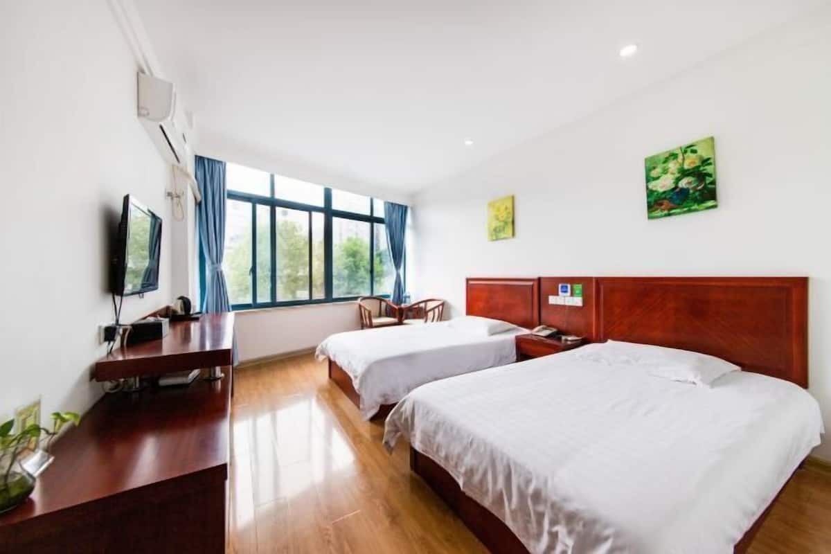 A hotel room with two beds, a desk with a TV, and a window with curtains.