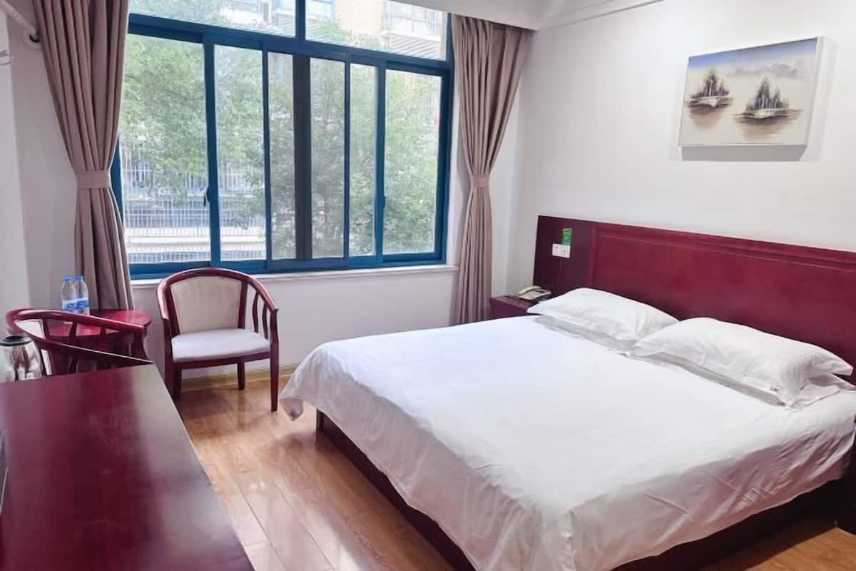 A hotel room with a bed, a chair, a desk, and a window with curtains.
