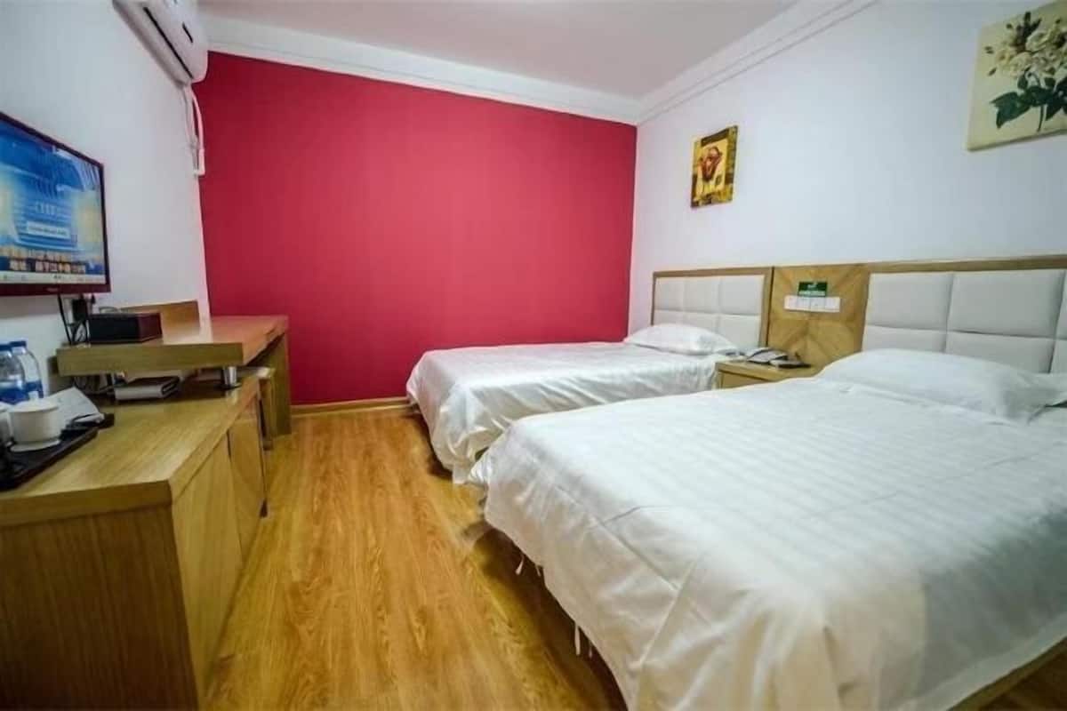 A hotel room with two beds, a desk, a television, and a red accent wall.