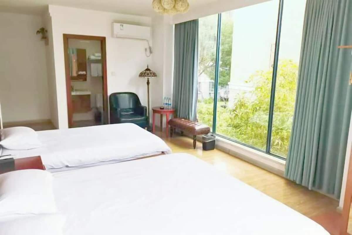 A hotel room with two beds, a chair, a small table, and a view of greenery outside.