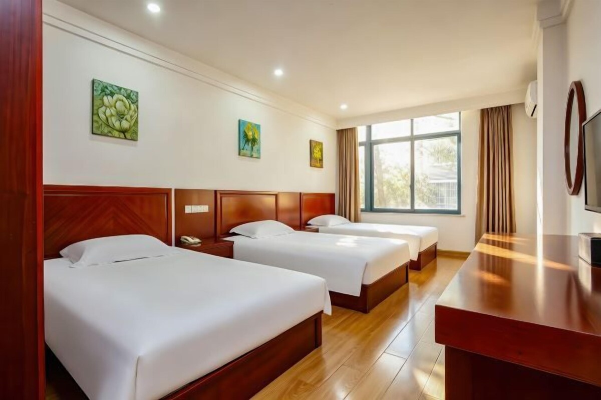 A hotel room with three beds, a wooden desk, and a large window.