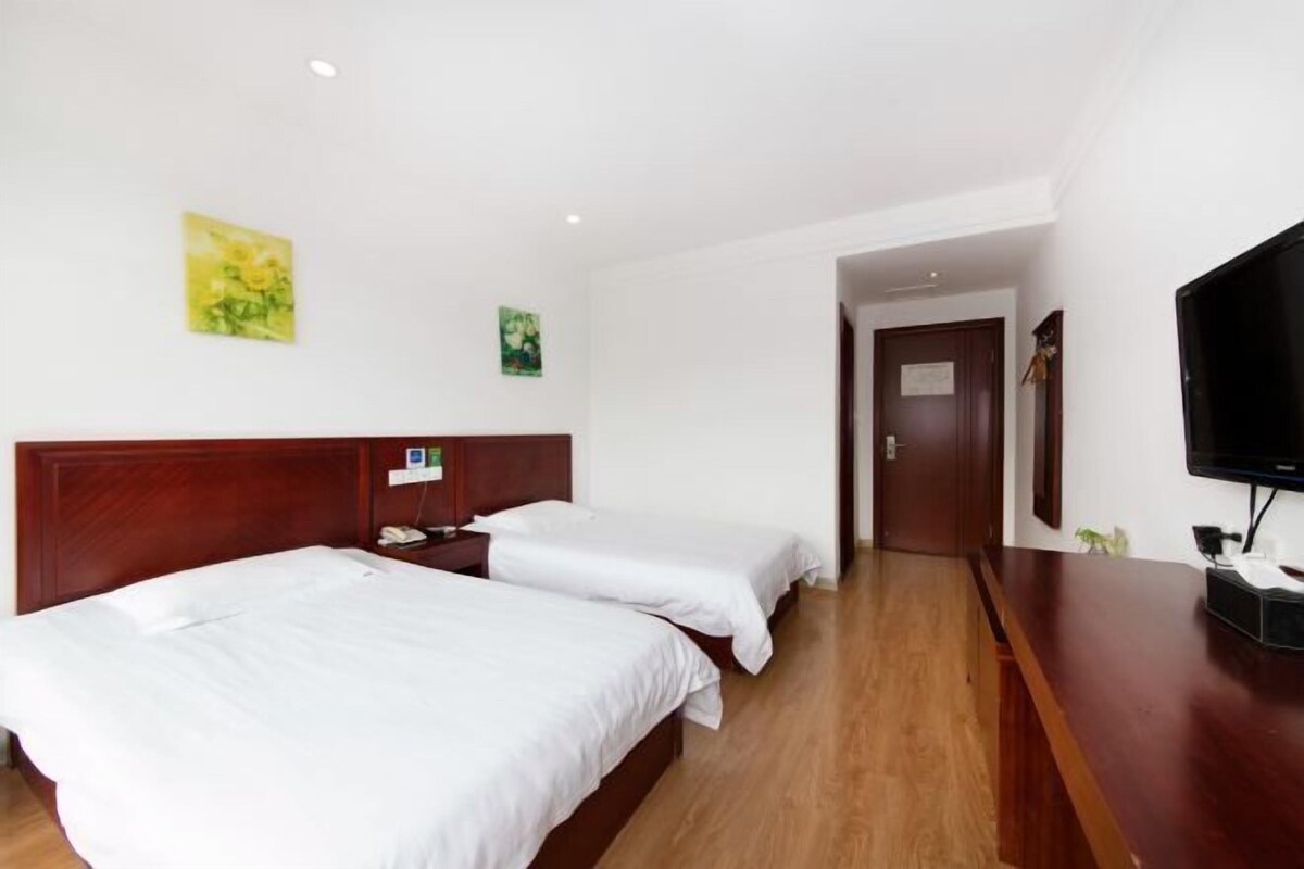 A hotel room with two beds, a wooden headboard, a flat-screen TV, and artwork on the walls.