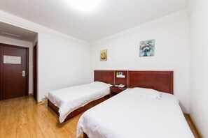 A hotel room with two single beds, a wooden headboard, a nightstand, and a small painting on the wall.