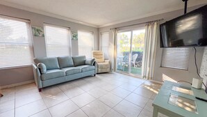 Ein Wohnzimmer mit einer Couch, einem Sessel, einem Fernseher und einem Tisch.