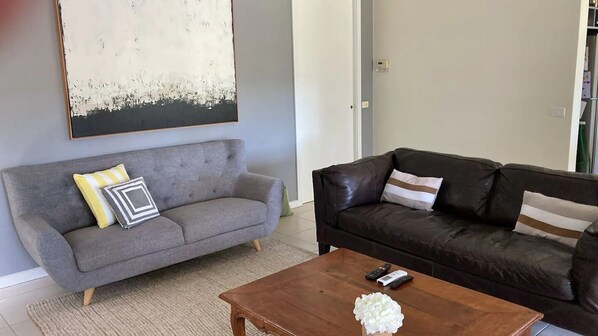 A living room with a grey sofa, a brown coffee table, and a black leather sofa.