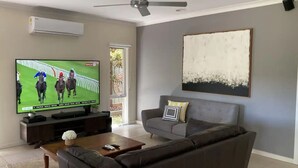 Un salon avec un téléviseur à écran plat, un canapé gris et un tableau accroché au mur.