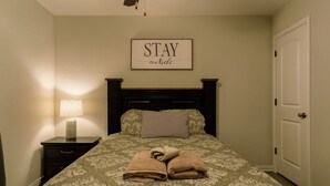 A neatly made bed with a patterned bedspread, a bedside lamp, and a framed sign on the wall. - 29-day min stays, In-unit laundry, and reliable WiFi. Corporates stays welcome (Bel Aire)
