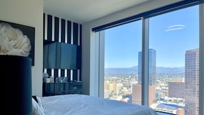 Un dormitorio moderno con una cama grande, un aparador oscuro y un ventanal con vistas a la ciudad.