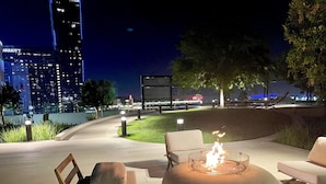 Un área de estar al aire libre con una chimenea, sillas y vistas de la ciudad de noche.