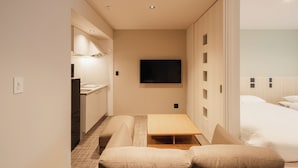 A compact hotel room with a kitchenette, a bed, a TV, and a sliding door leading to a bathroom. - HOTEL SHUTEC (Kagoshima)