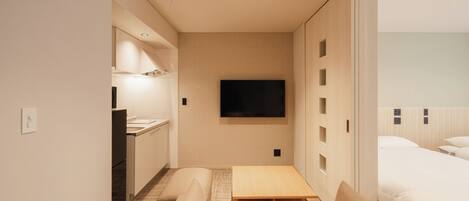 Una camera d'albergo compatta con angolo cottura, un letto, una TV e una porta scorrevole che dà accesso al bagno.