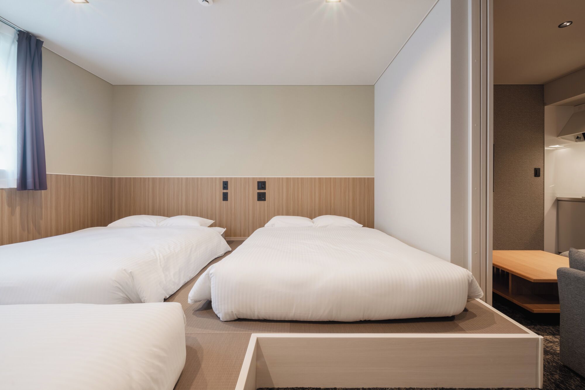 A hotel room with two beds, a wooden headboard, a small table, and a chair.