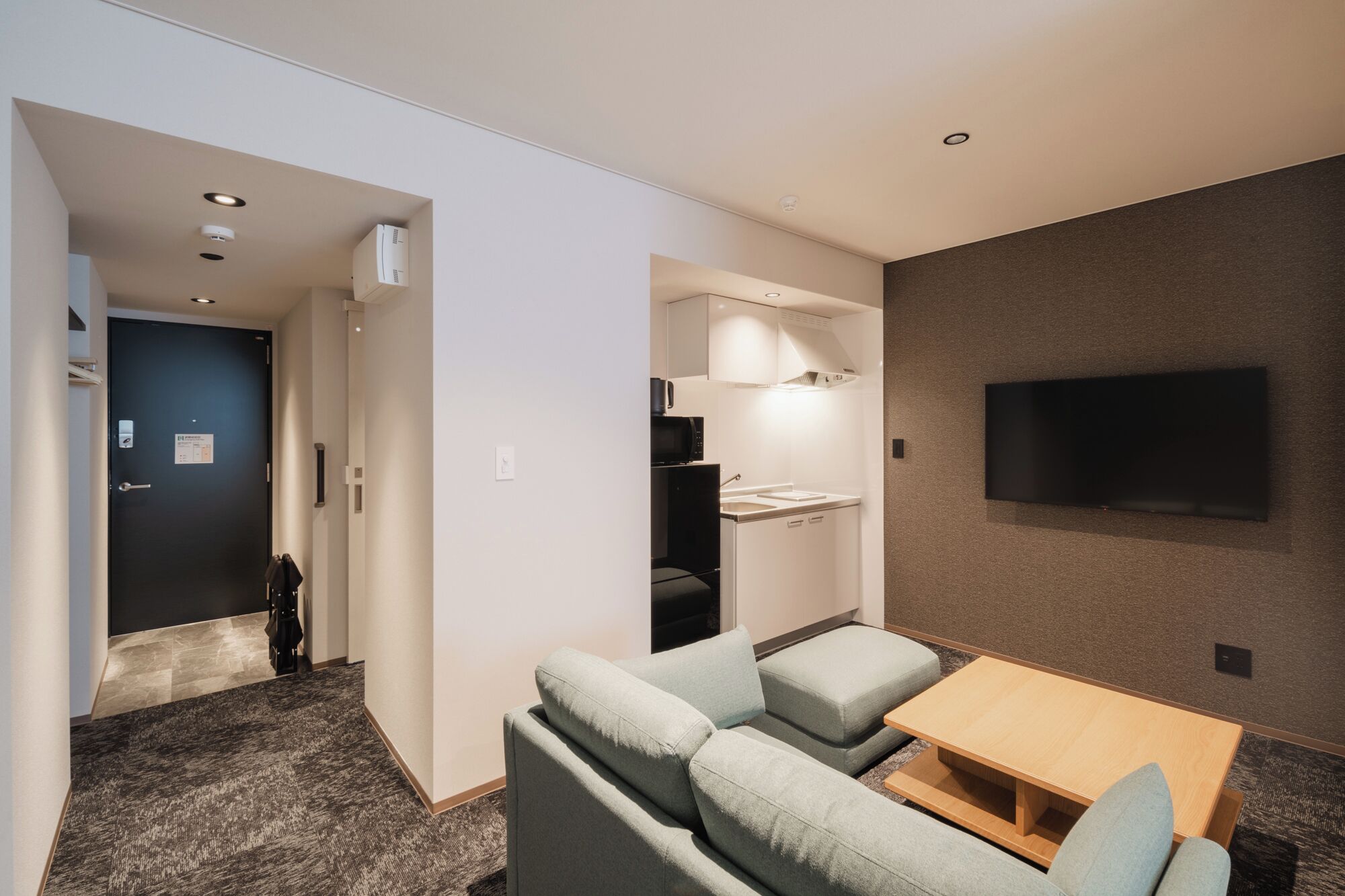 Quarto de hotel com sofá, uma mesinha, TV fixada na parede, micro-ondas e frigorífico.