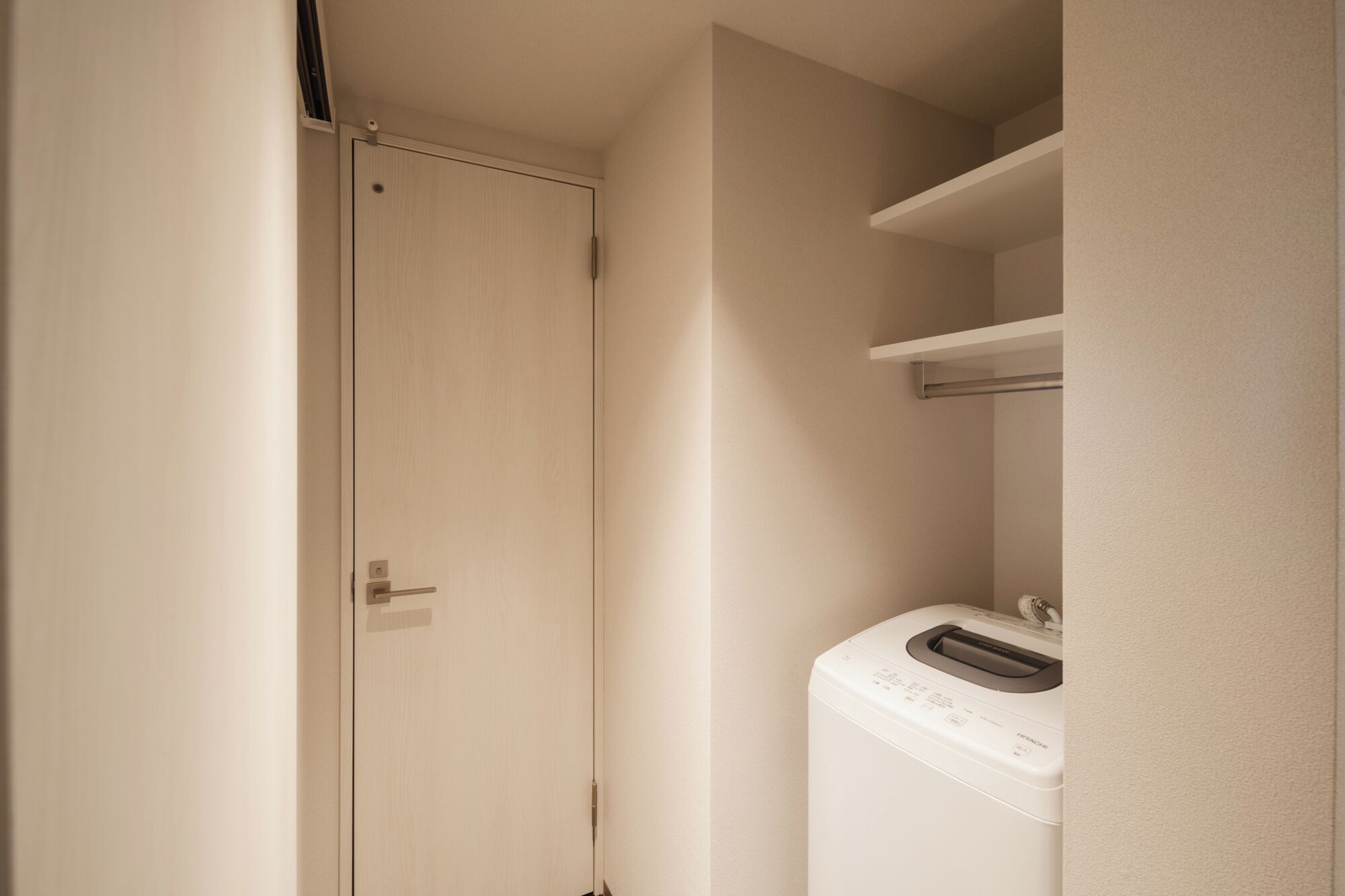 A laundry room with a washing machine, a closed door, and a shelf.