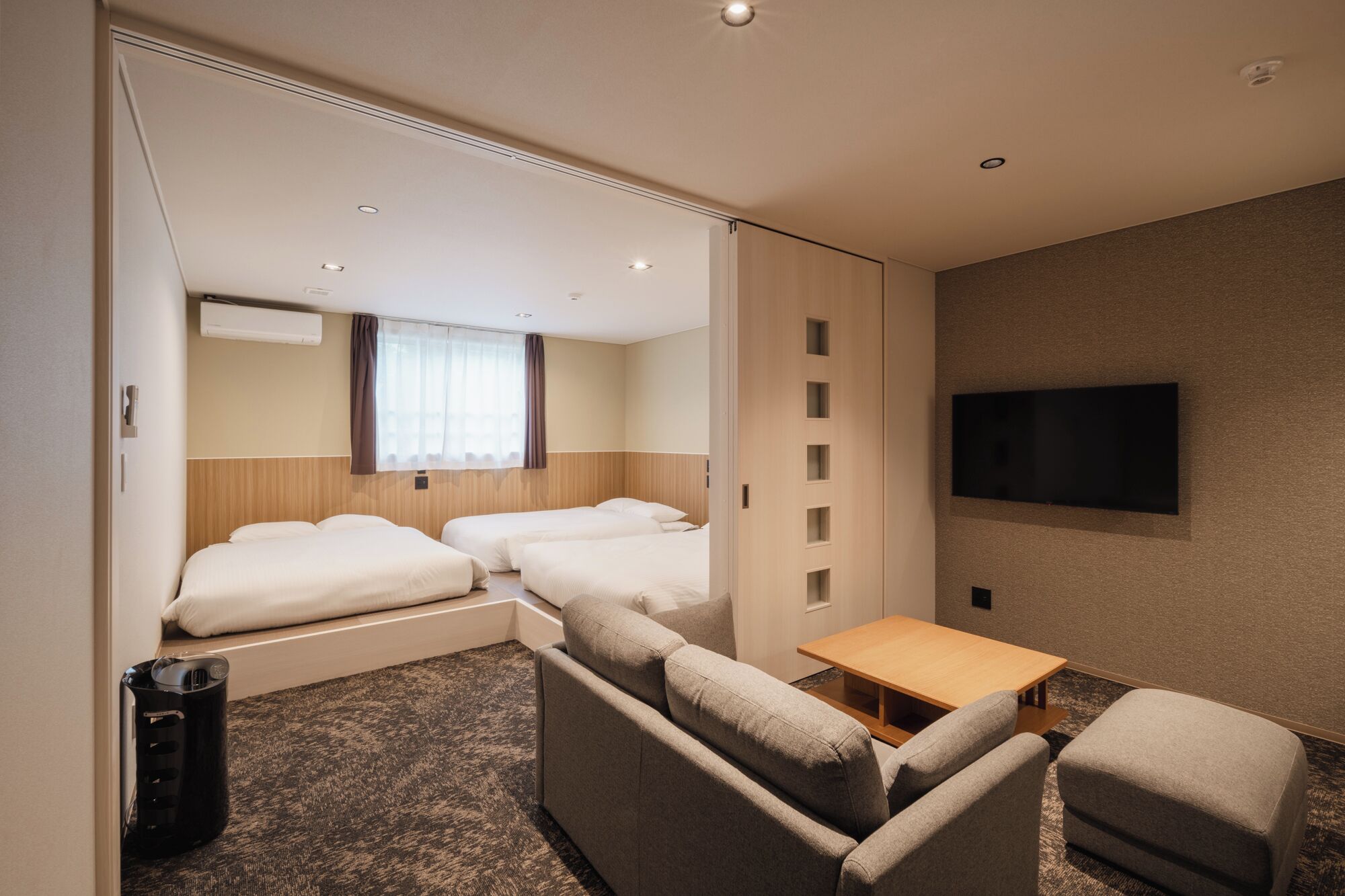 A hotel room with two beds, a sofa, a TV, and a small table.