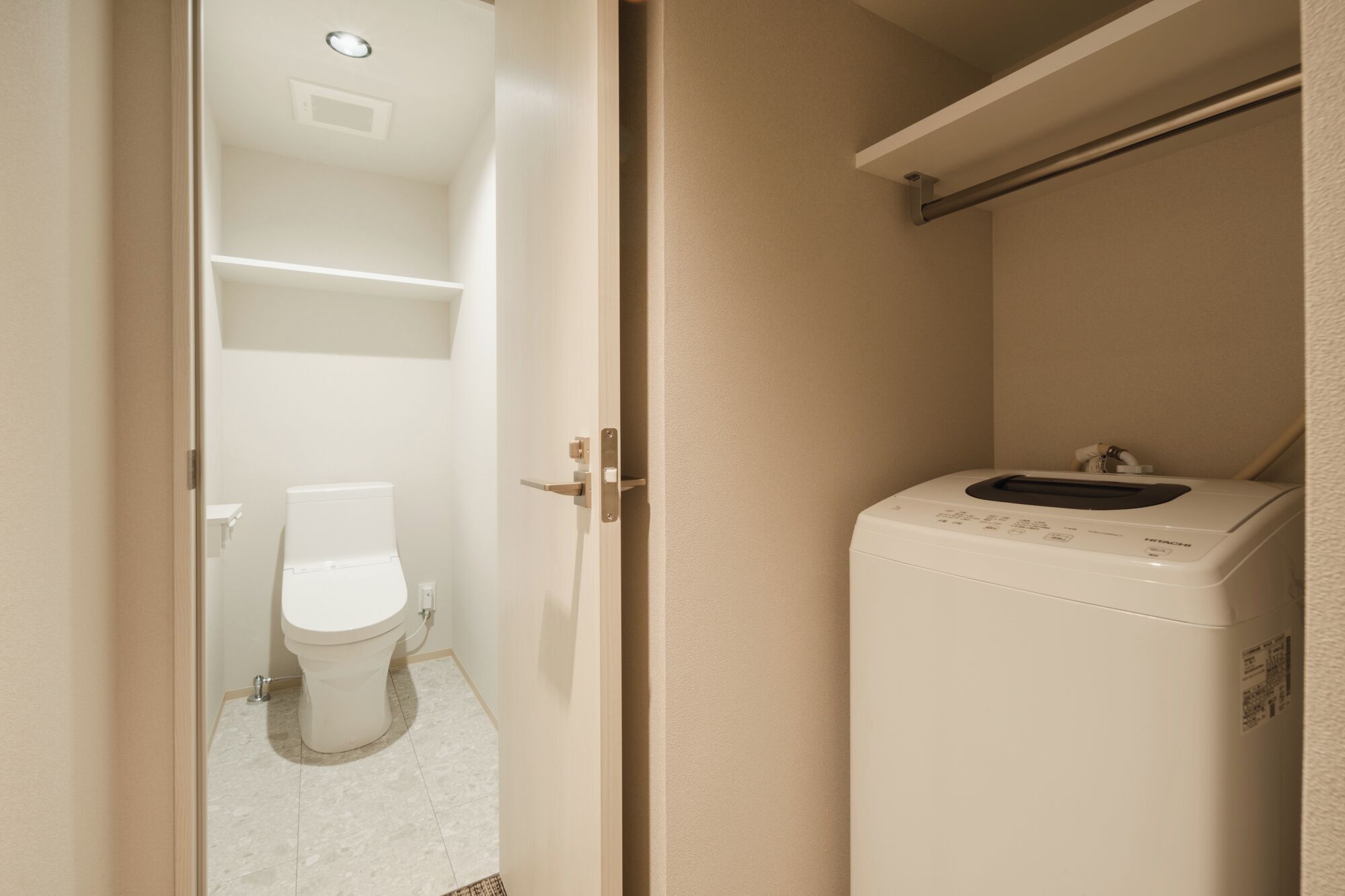A compact bathroom with a toilet, a washing machine, and a shelf above the machine.