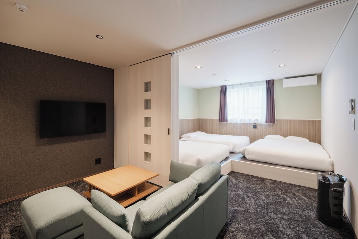 Ein Hotelzimmer mit einer Couch, einem kleinen Tisch, einem Fernseher, zwei Betten, einem Spiegel und einem Mülleimer.
