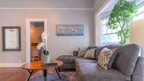 A living room with a grey sofa, a round coffee table, and a painting of sailboats on the wall. - High Ceiling, Cozy 1BR Apt, Walk to Metro & Shops (Pasadena)