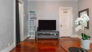 A living room with a flat-screen TV, a white door, a potted orchid, and a remote control on a black mat. - High Ceiling, Cozy 1BR Apt, Walk to Metro & Shops (Pasadena)